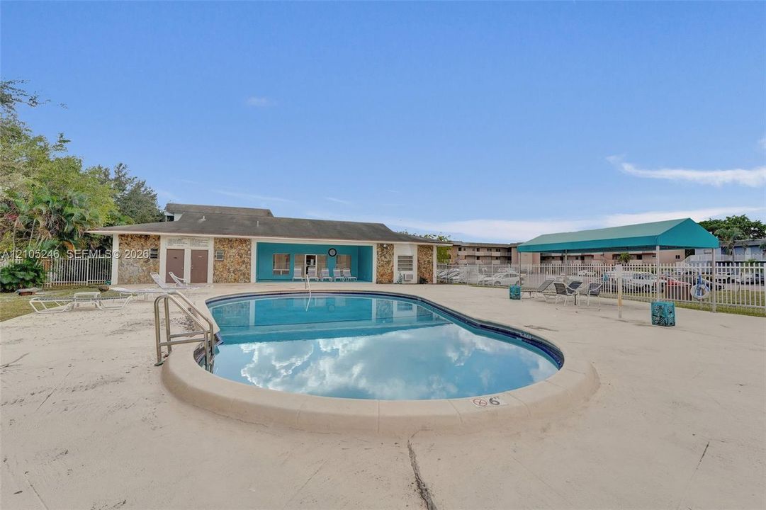 In-ground pool featuring a concrete deck, metal handrail, and shaded canopy area