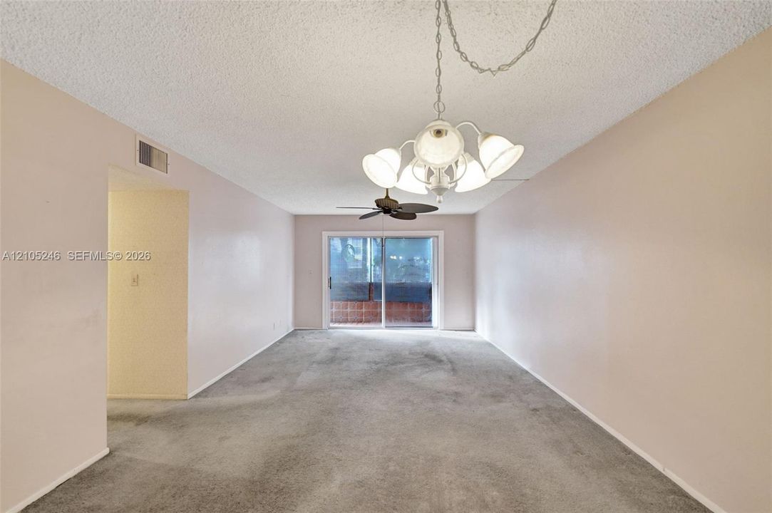 Interior space featuring a multi-arm chandelier with frosted glass shades, a ceiling fan, carpeted flooring, and a sliding glass door