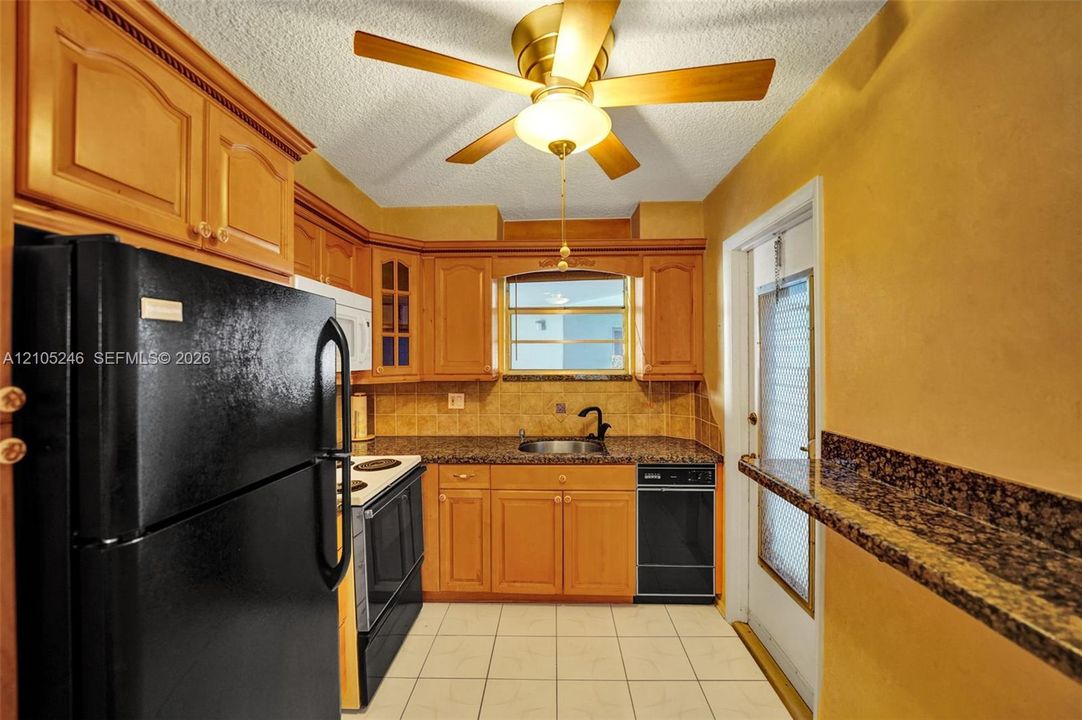 Kitchen featuring wood cabinetry, stone-finish countertops, tile backsplash, tile flooring, and ceiling fan with integrated light fixture