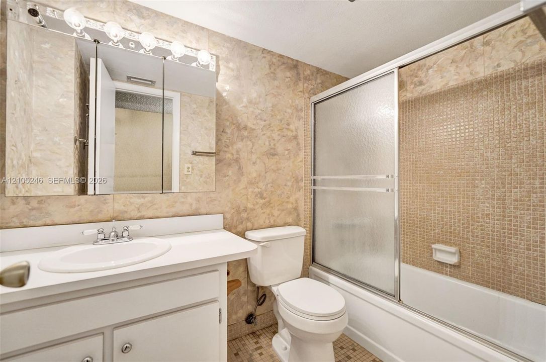 Bathroom featuring a white vanity with an integrated sink, tri-fold medicine cabinet, five-light fixture, and a bathtub with sliding glass doors and tiled surround