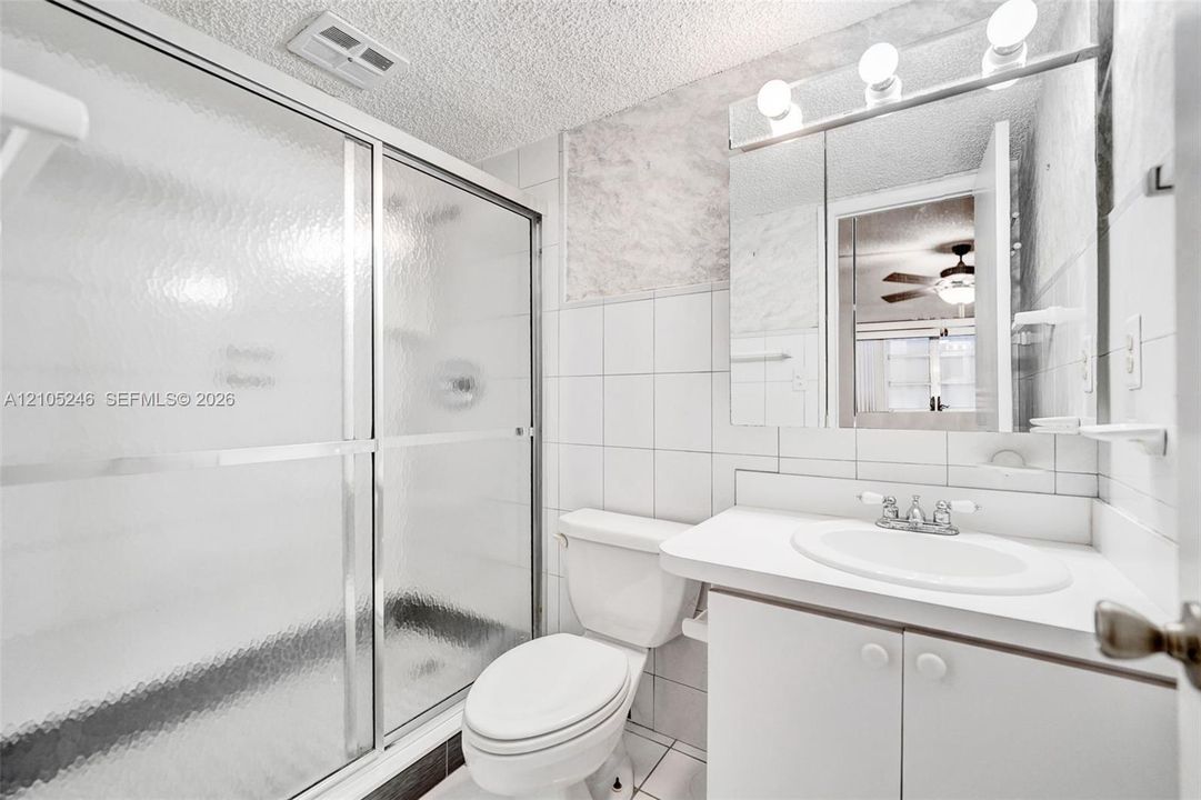 Bathroom featuring a shower with a textured glass sliding door, integrated vanity with a basin sink, expansive wall-mounted mirror, and wall-mounted light fixture