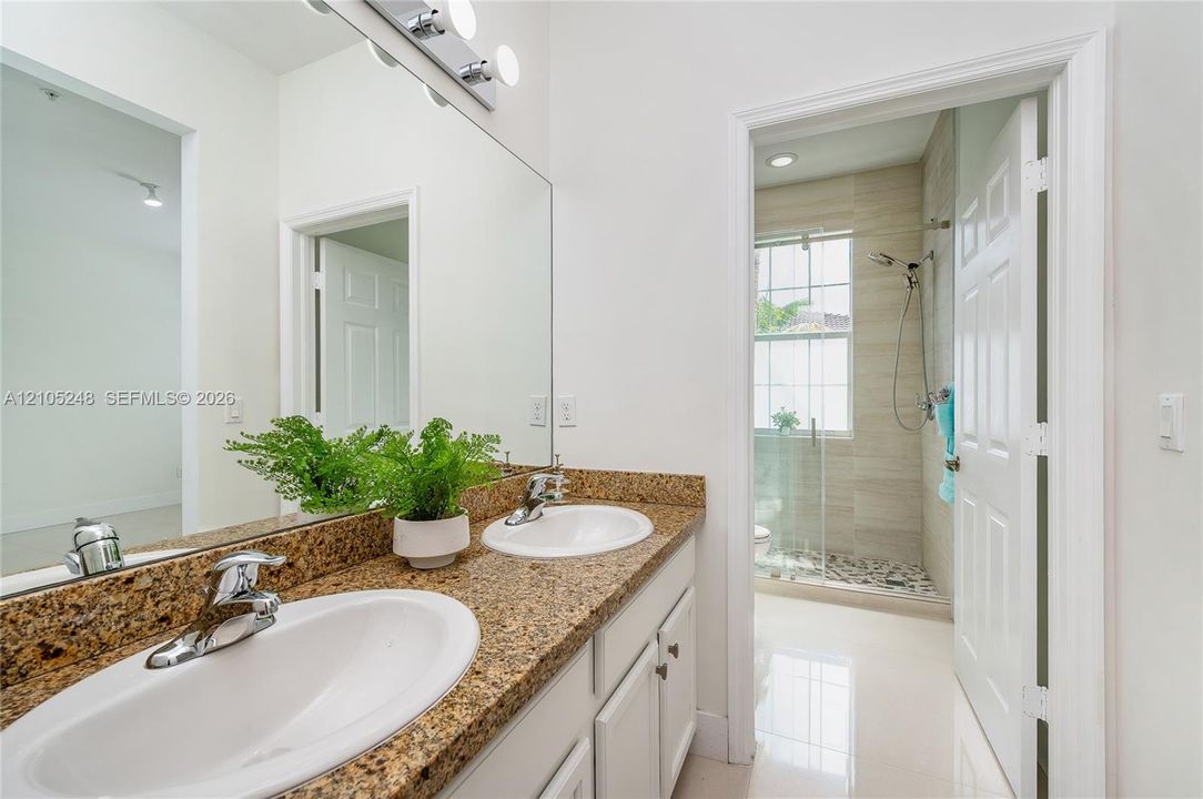 Dual vanity with granite countertop, white cabinetry, and chrome fixtures