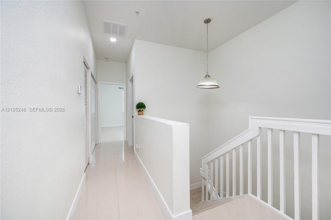 Hallway featuring light-toned flooring, white walls, and a contemporary pendant light fixture