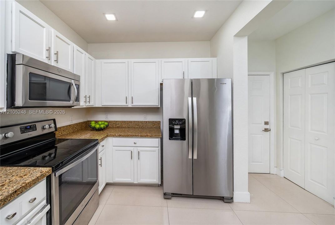 Kitchen featuring white cabinetry, stainless steel appliances, granite countertops, and light-colored floor tiles