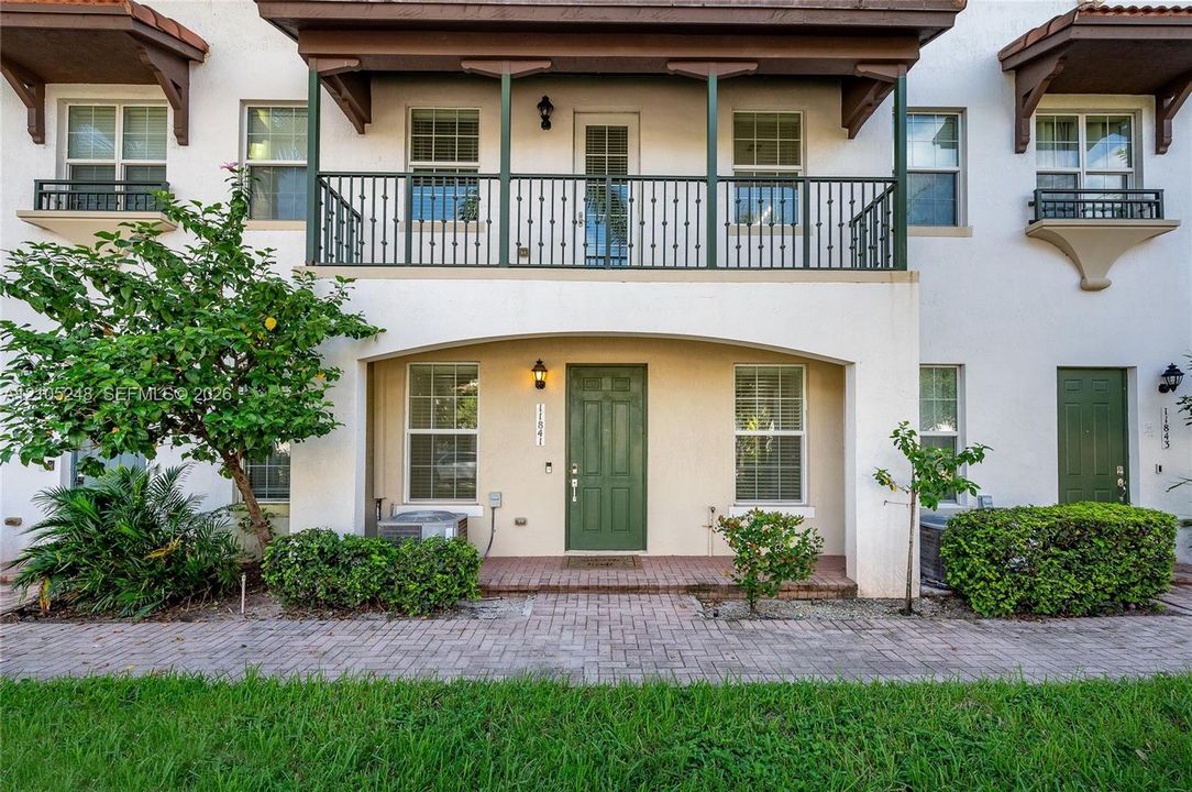 Stucco exterior with a tiled roof accent, featuring a ground-level covered entry, a second-story balcony with metal railings, and a decorative Juliet balcony