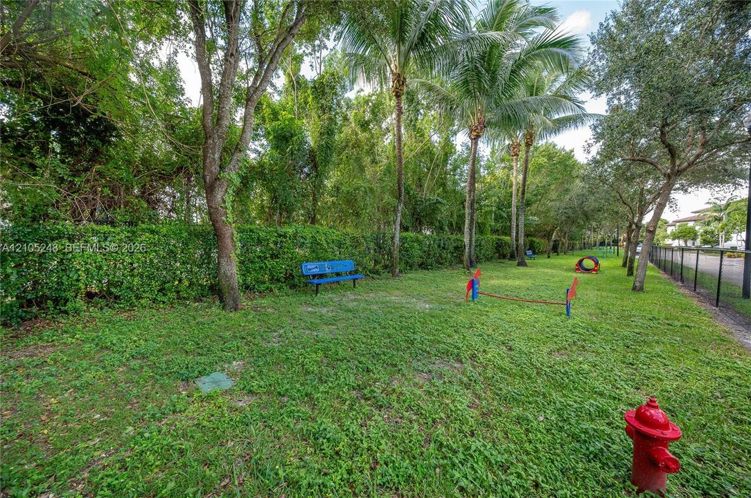 Expansive grassy area featuring mature trees, a blue park bench, and a black wire fence