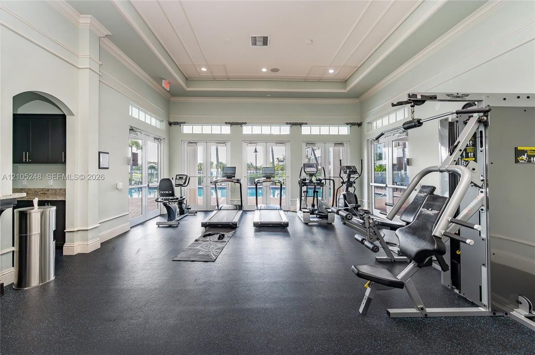 Spacious fitness center featuring a coffered ceiling, multiple French doors, transom windows, and a built-in counter with dark cabinetry