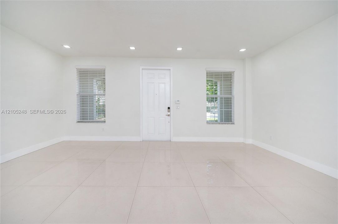 Recessed ceiling lighting, two windows with blinds, light-toned tile flooring, and a white paneled door