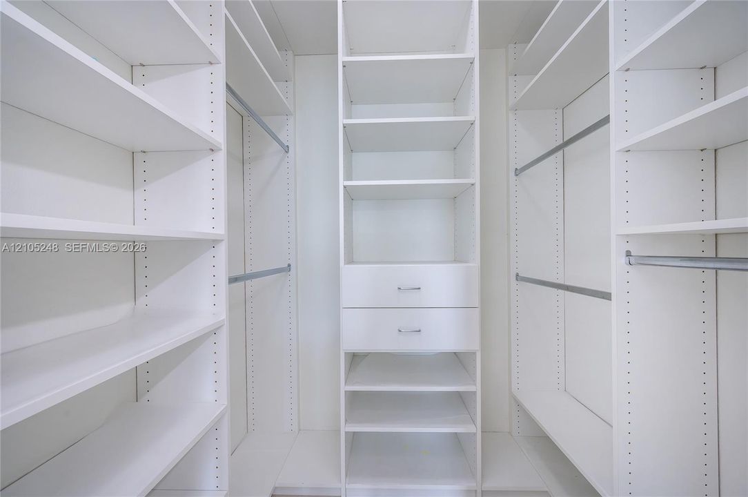 Custom closet system featuring white shelving, hanging rods, and integrated drawers with polished hardware