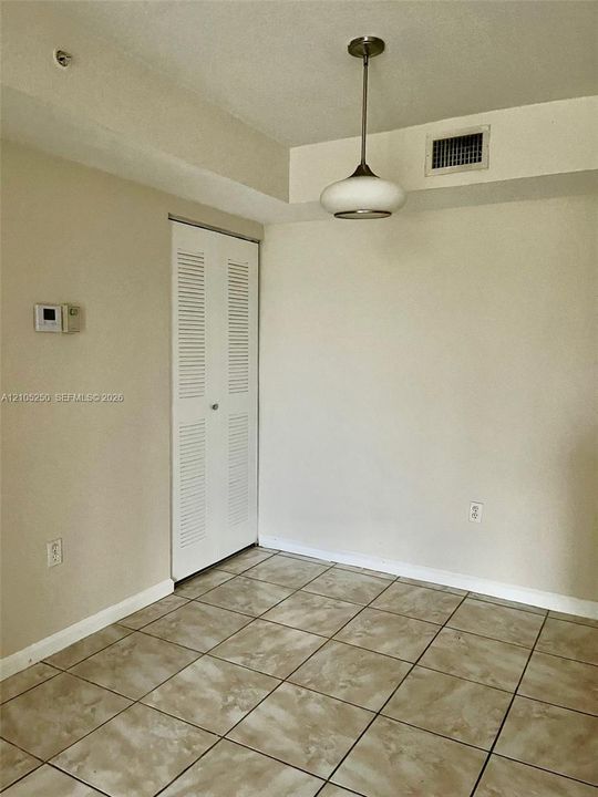 Neutral toned tile flooring, louvered bi-fold closet door, and a suspended ceiling light fixture