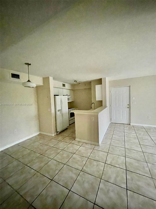 Open-concept living area with neutral tile flooring, kitchen featuring a white refrigerator and range, and a built-in breakfast bar