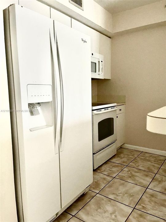 Kitchen featuring tile flooring, white side-by-side refrigerator, white microwave, white electric range, and light-toned cabinetry