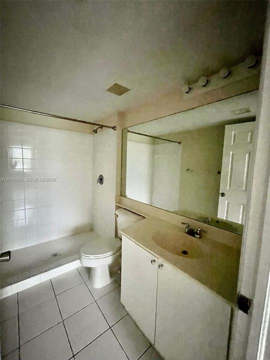 White tiled flooring, vanity with integrated sink, large wall-mounted mirror, and white subway-tiled shower
