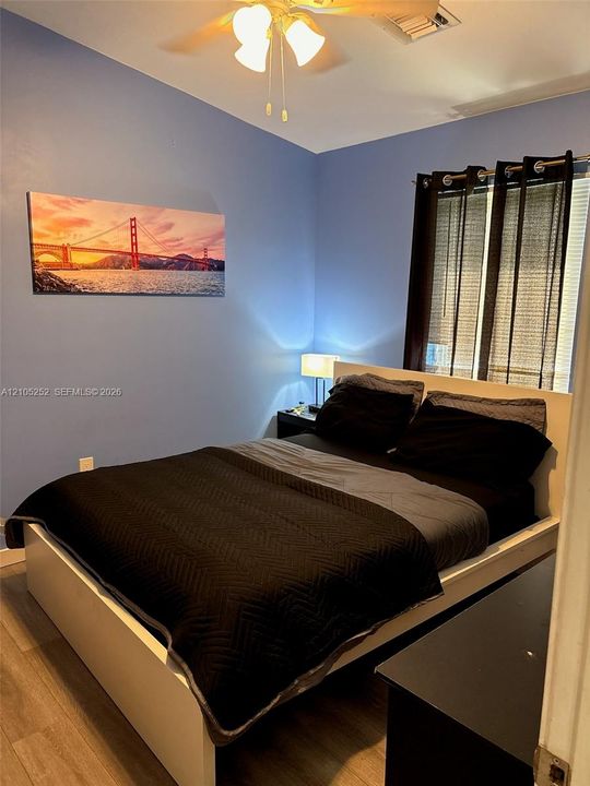 Wood-finish flooring, ceiling fan with integrated lighting, window with blinds, and painted walls