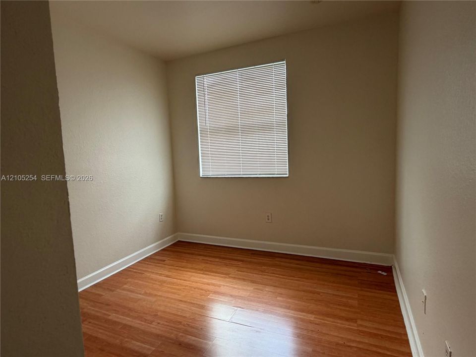 Wood-finish flooring with white baseboards, textured walls, and a window with horizontal blinds
