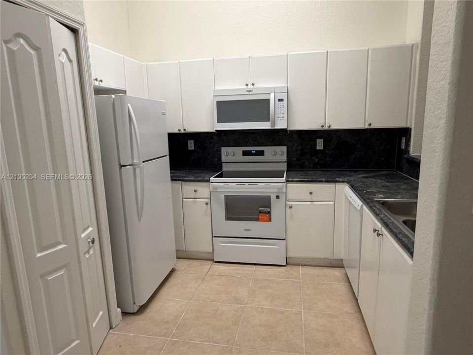 Kitchen featuring white cabinetry, dark countertops, white refrigerator, and a white range with an above-range microwave