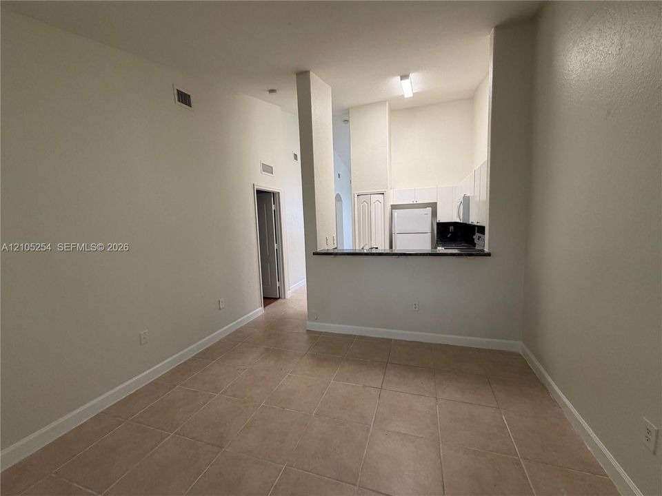 Neutral-toned tile flooring, white walls, and a kitchen pass-through with a dark countertop