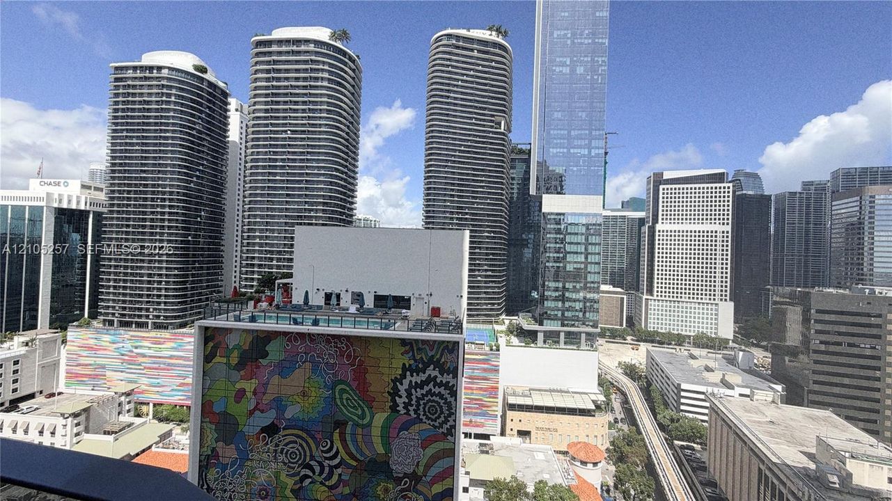 Urban cityscape featuring high-rise architecture, decorative exterior mural, and elevated rail infrastructure