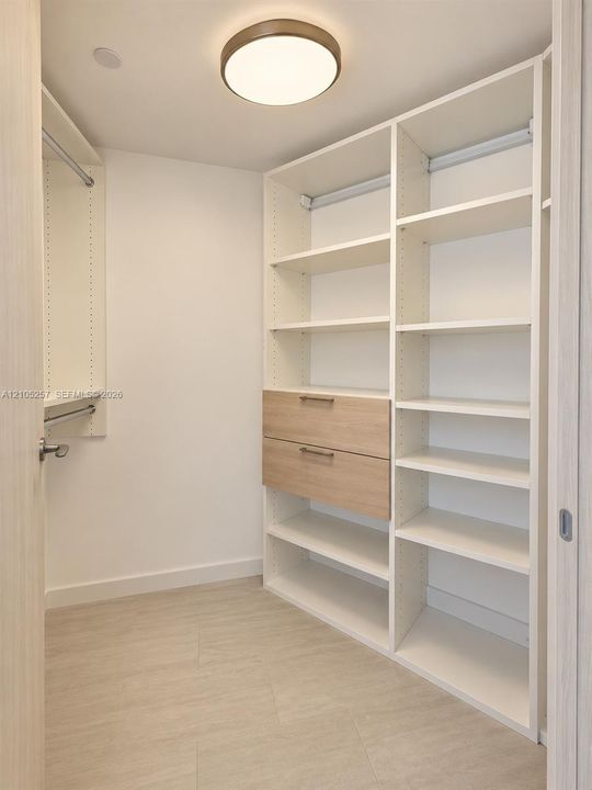 Custom storage closet featuring adjustable shelving, integrated drawers with metallic pulls, dual hanging rods, and a flush-mount circular overhead light fixture