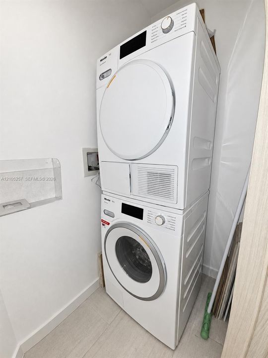 Stacked white front-loading laundry unit with integrated control panels and recessed wall shelving