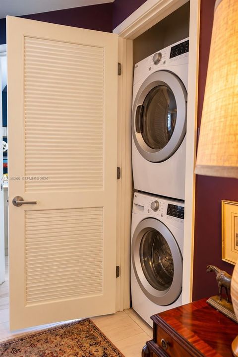 Stacked laundry unit featuring a white louvered privacy door with a satin nickel lever handle