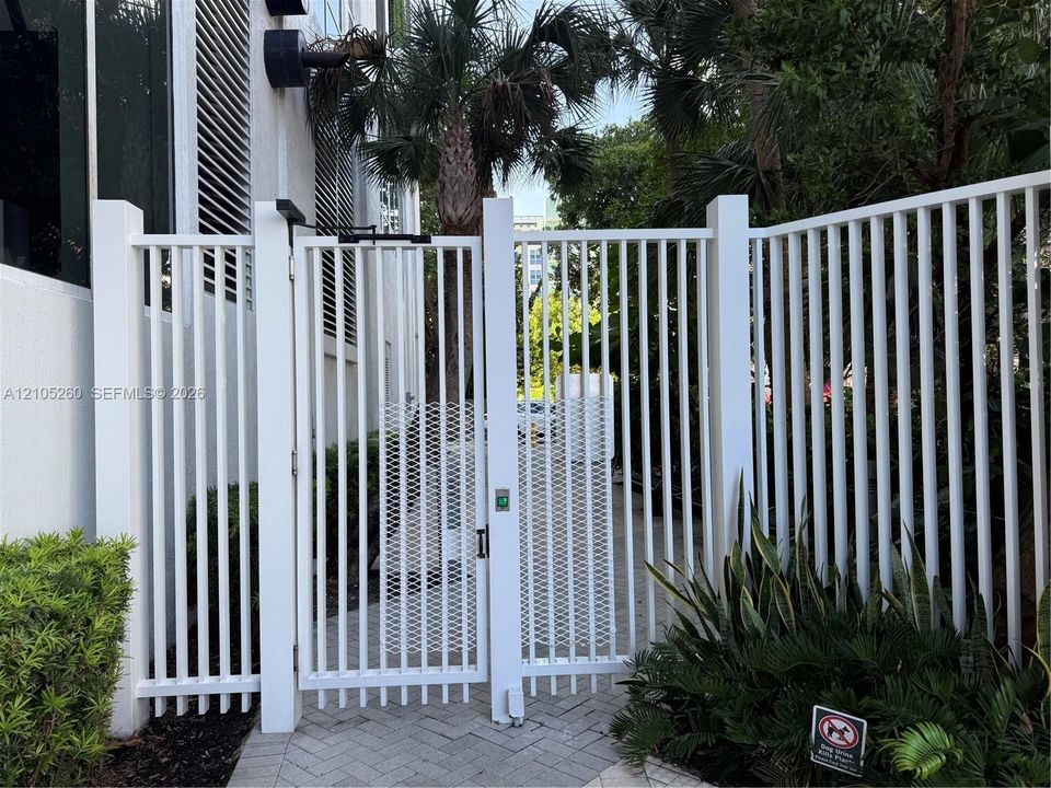 White vertical picket fencing featuring a secure metal gate with integrated electronic access panel and paver stone walkway