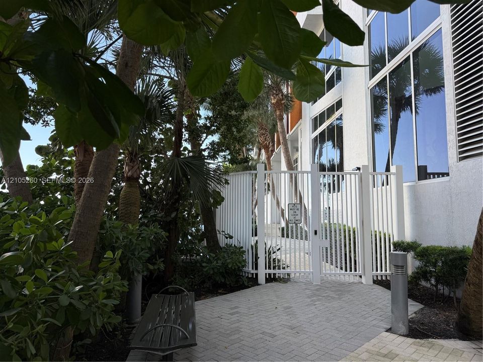 Exterior featuring multi-story glass windows, white vertical slat gating, paver hardscaping, and mature palm trees
