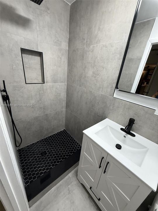 Tiled shower with a recessed niche, black hexagon tile flooring, and a rainfall showerhead