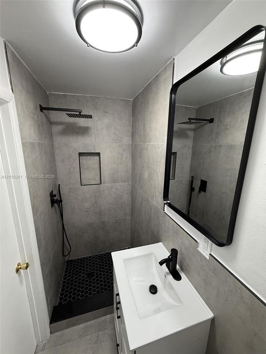 Tiled shower with a rainfall showerhead, recessed niche, and black hexagonal floor tiles