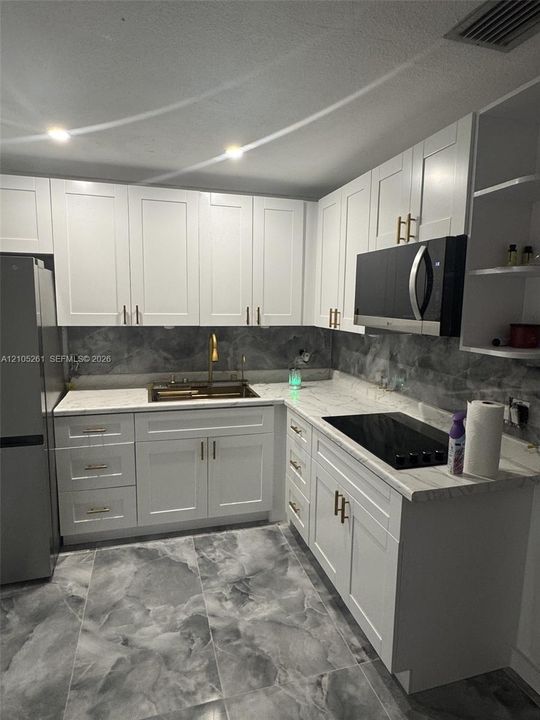 Kitchen featuring white shaker cabinetry, light-toned countertops, a built-in microwave, and a flush-mounted cooktop