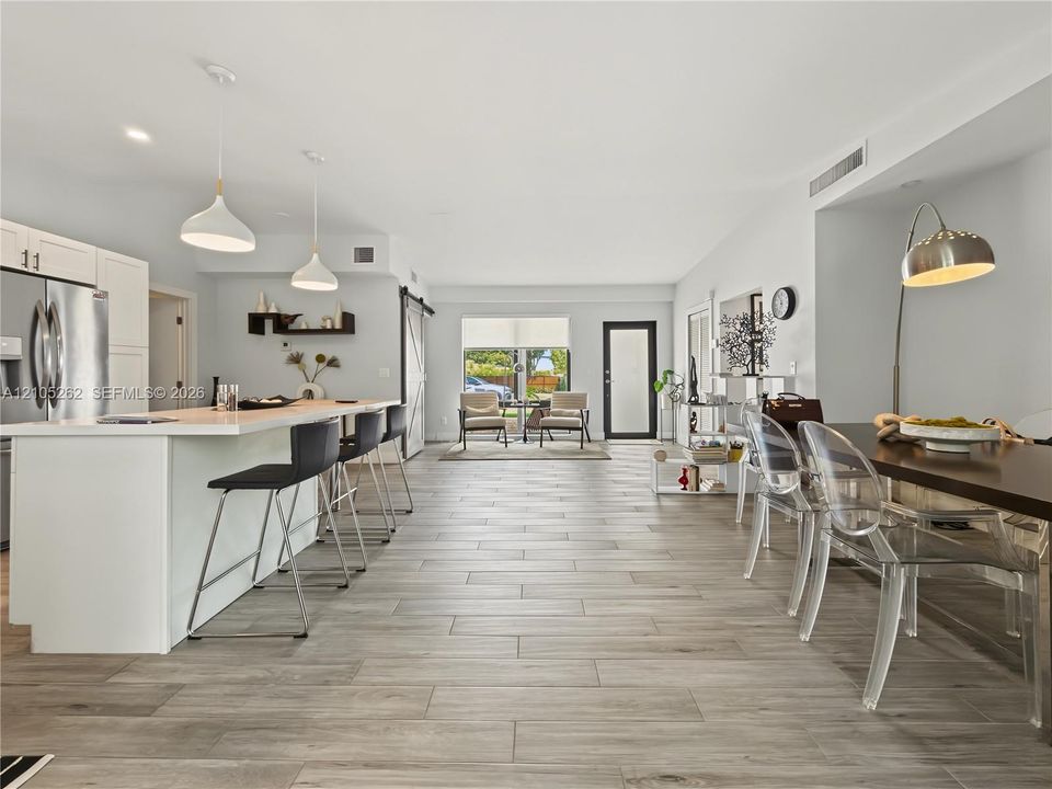 Open concept layout with wood-finish flooring, white kitchen cabinetry, stainless steel refrigerator, and a kitchen island with seating