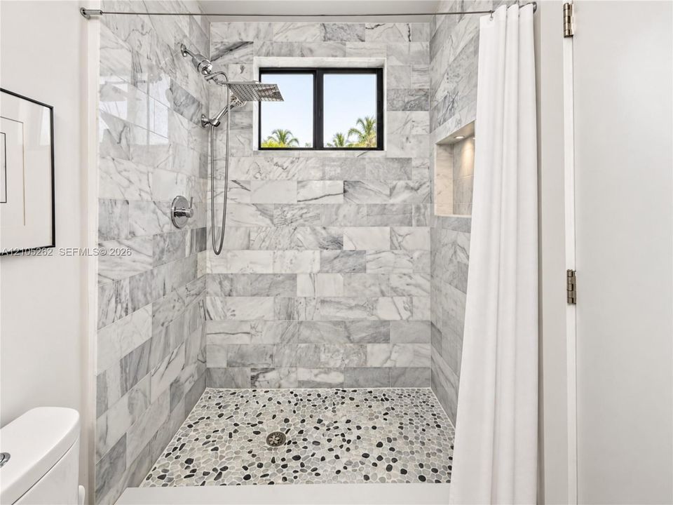 Tiled shower with a rainfall showerhead, handheld sprayer, built-in recessed niche, and pebble-style floor