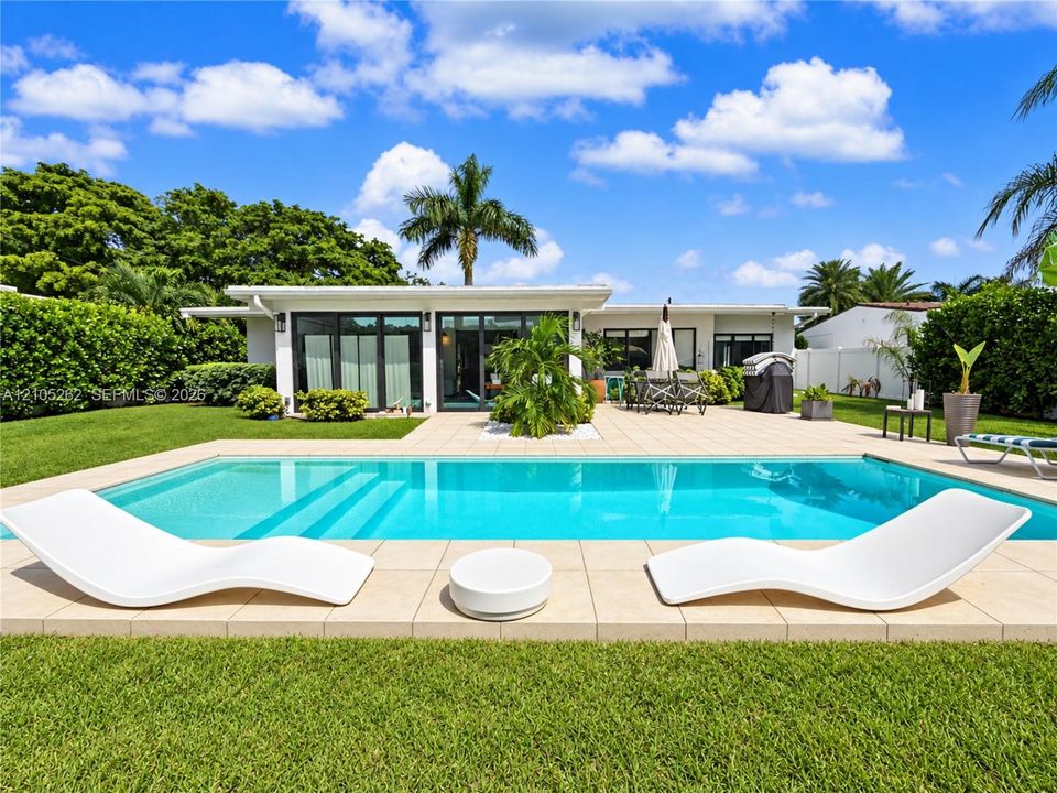 Rectangular swimming pool with integrated steps, surrounded by a paved patio and green lawn