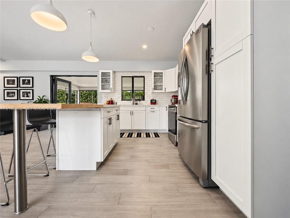 Contemporary kitchen featuring white cabinetry, stainless steel appliances, a center island with a wood-finish countertop, pendant lighting, and light-toned tile flooring