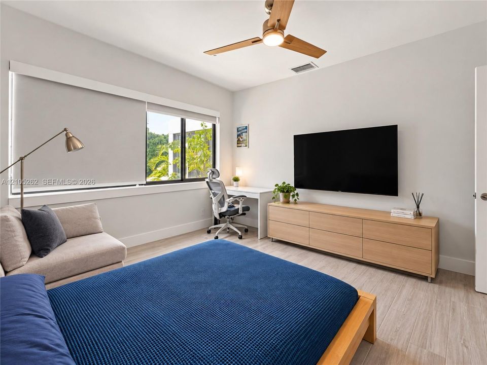 Wood-finish flooring, contemporary ceiling fan, wide window with roller shades, and a built-in media console