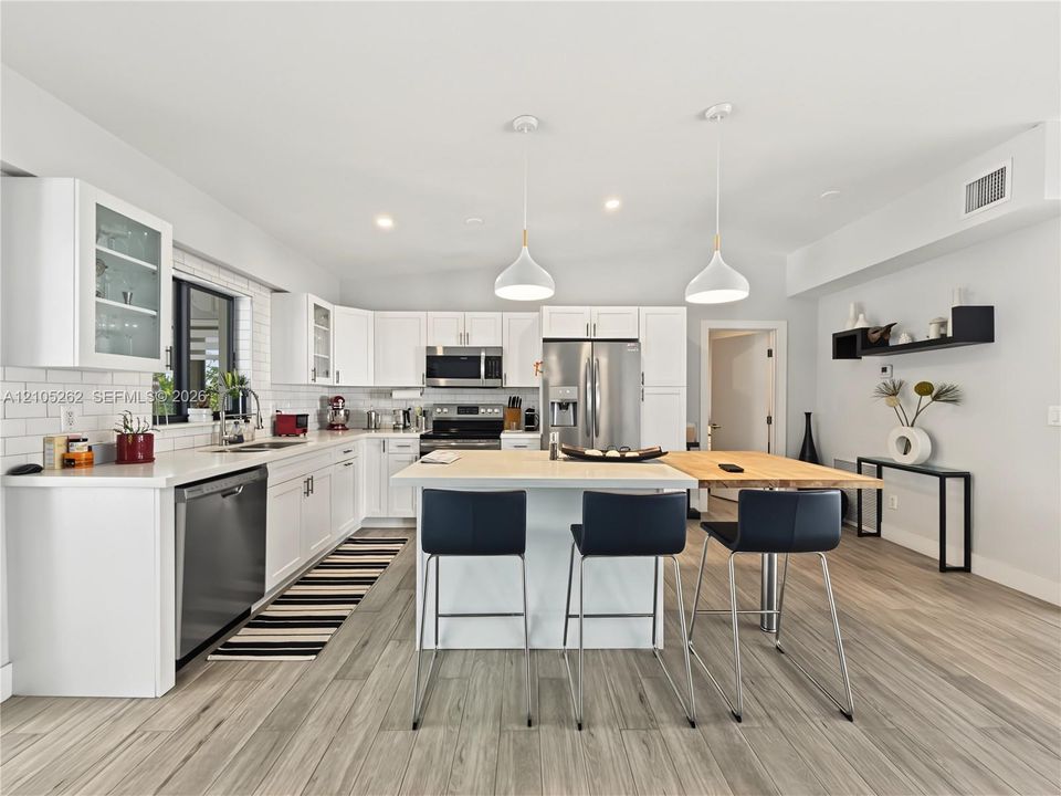 Kitchen featuring white cabinetry, subway tile backsplash, stainless steel appliances, a center island with seating, and wood-finish flooring