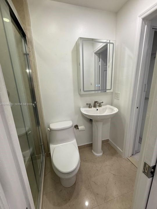 Pedestal sink with polished chrome fixtures, white two-piece toilet, illuminated medicine cabinet, and glass-enclosed shower