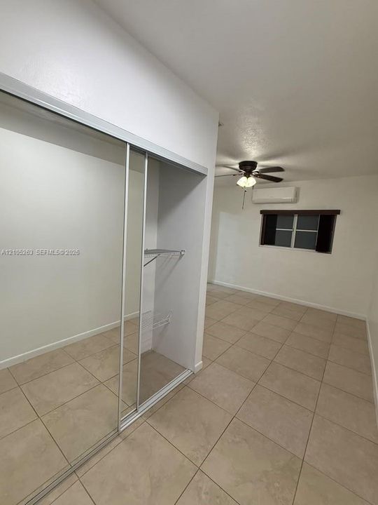 Neutral-toned tile flooring, mirrored sliding closet doors, built-in closet shelving, ceiling fan, and wall-mounted air conditioning unit