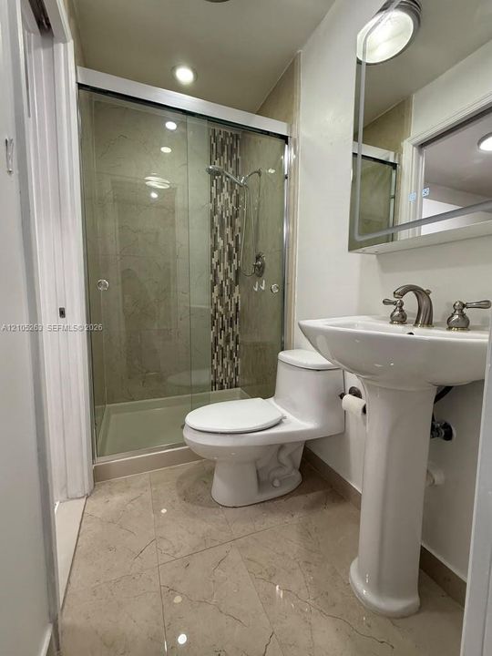Glass-enclosed shower with a tiled accent wall, pedestal sink, and large format floor tiling
