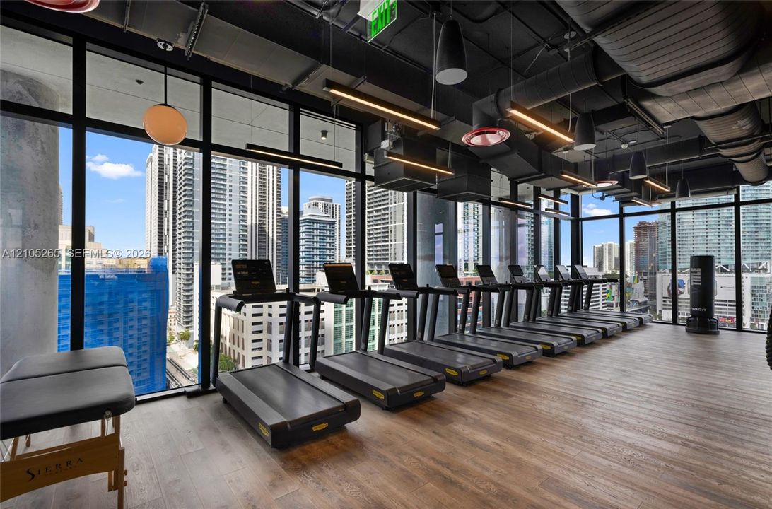 Fitness center featuring floor-to-ceiling windows, wood-finish flooring, exposed industrial-style ductwork, and suspended linear lighting