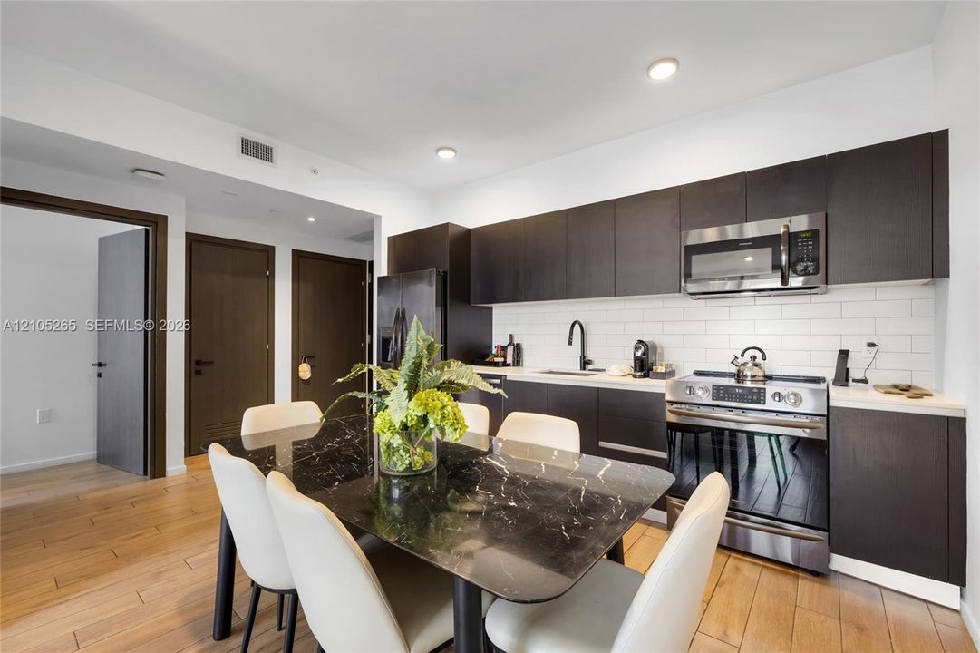 Kitchen featuring dark cabinetry, white subway tile backsplash, stainless steel appliances, and wood-finish flooring
