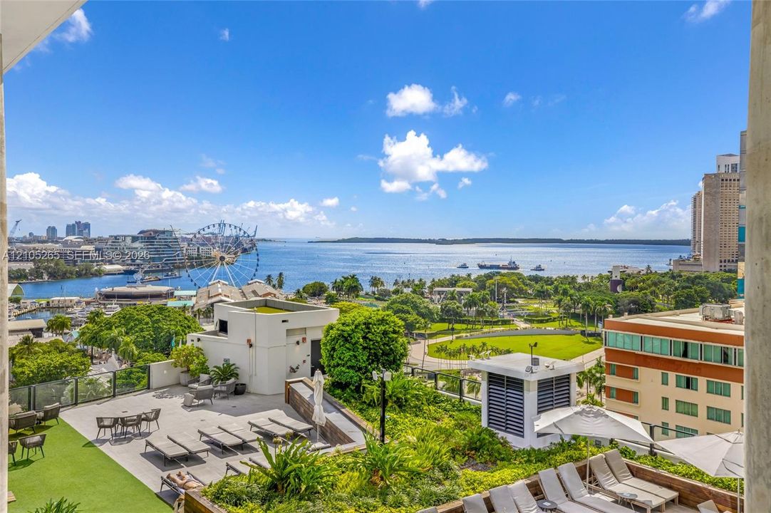 Elevated rooftop terrace featuring synthetic turf, stone-paver flooring, built-in planters, and panoramic water and urban harbor scenery