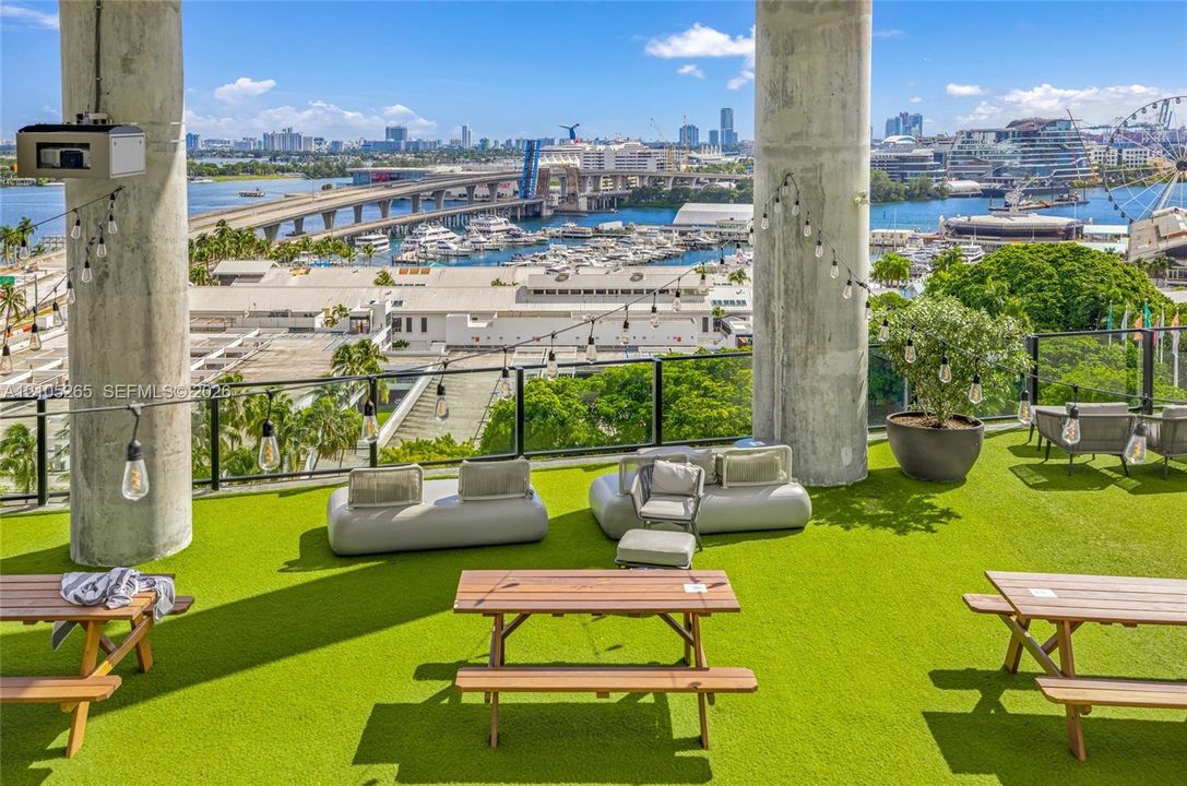Rooftop terrace featuring synthetic turf flooring, exposed structural concrete pillars, and a glass panel railing