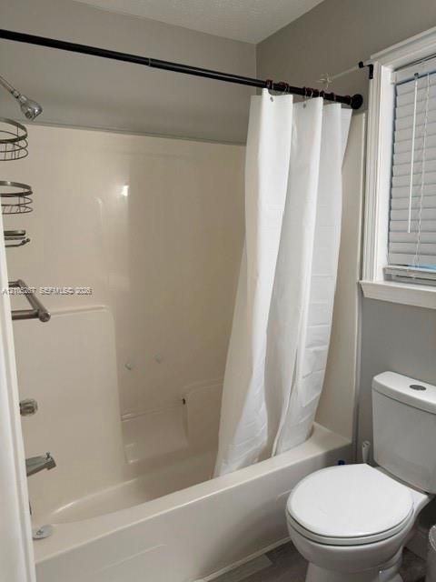 Integrated shower and bathtub combination with a chrome shower head and bath fixtures, adjacent to a white toilet with a matching tank and lid, set on wood-finish flooring