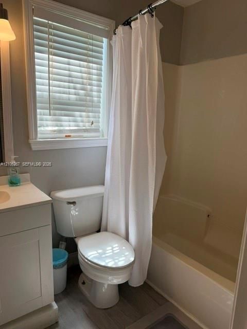 Window with horizontal blinds, white vanity with integrated sink, toilet, tub/shower combination, and wood-finish flooring