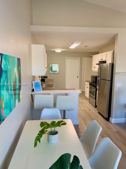 Kitchen featuring stainless steel appliances, wood-finish flooring, white cabinetry, a breakfast bar, and recessed lighting