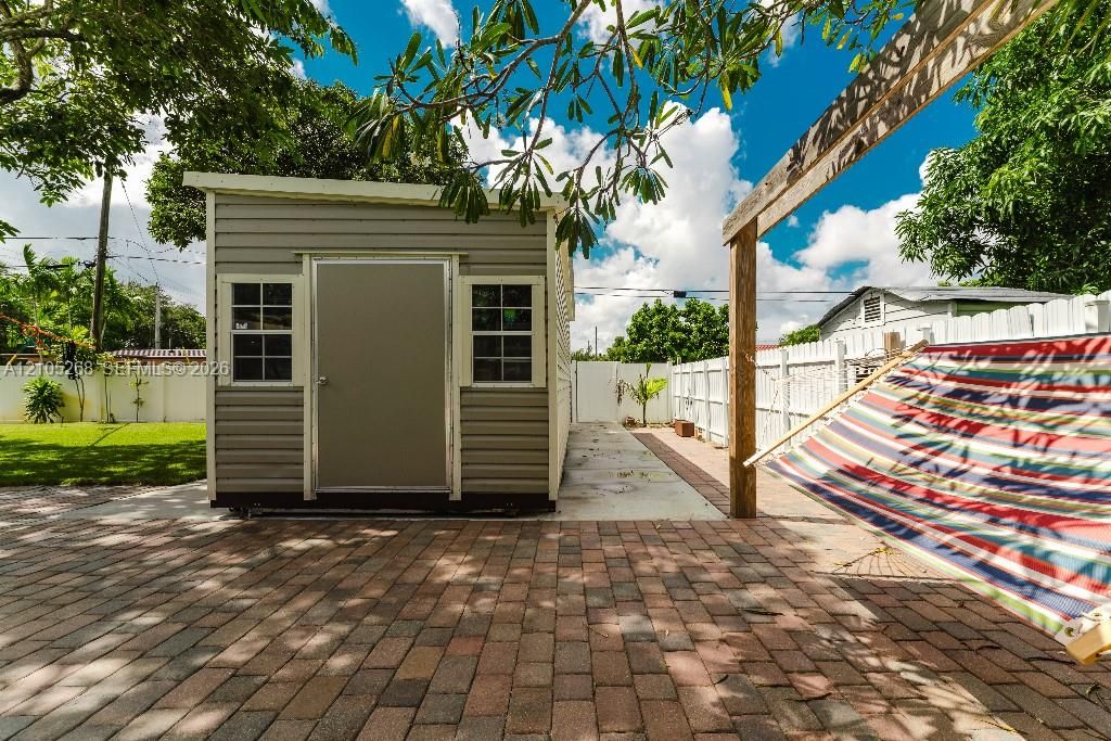 Brick paver patio, wood-beam pergola, and a storage shed with siding and windows