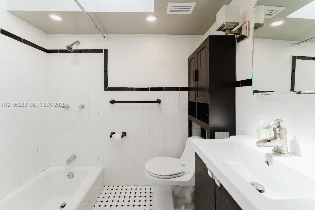 White subway tile with black trim, recessed lighting, black and white mosaic floor tile, white vanity with integrated sink, and dark wood-finish cabinet