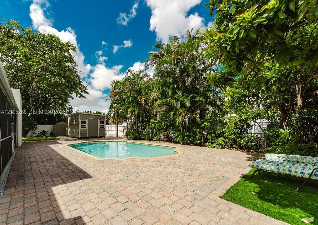 Paved patio with an in-ground pool, surrounded by mature trees and lush landscaping