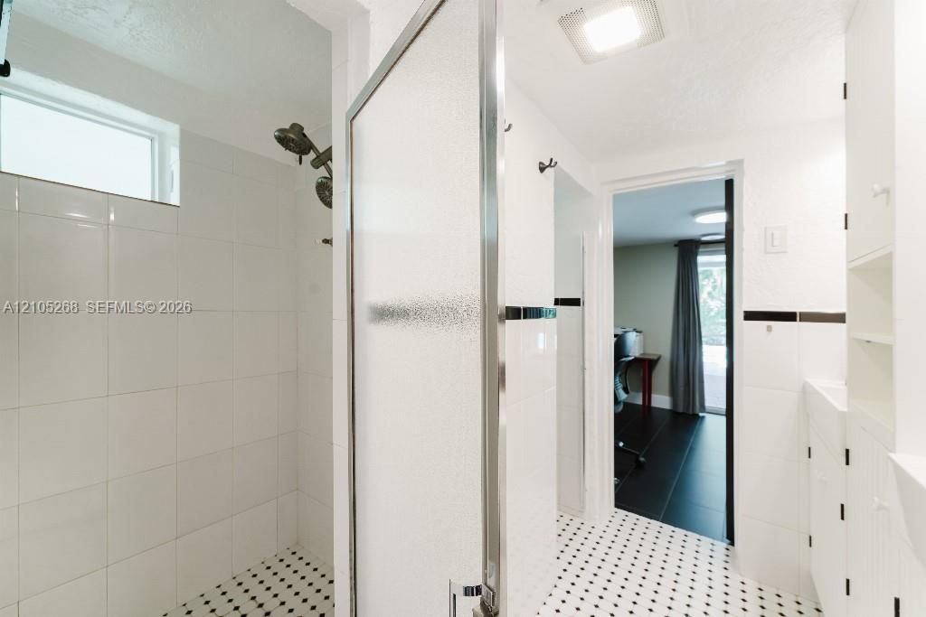 Shower enclosure with a satin nickel shower head, white subway tile surround, and mosaic tile flooring